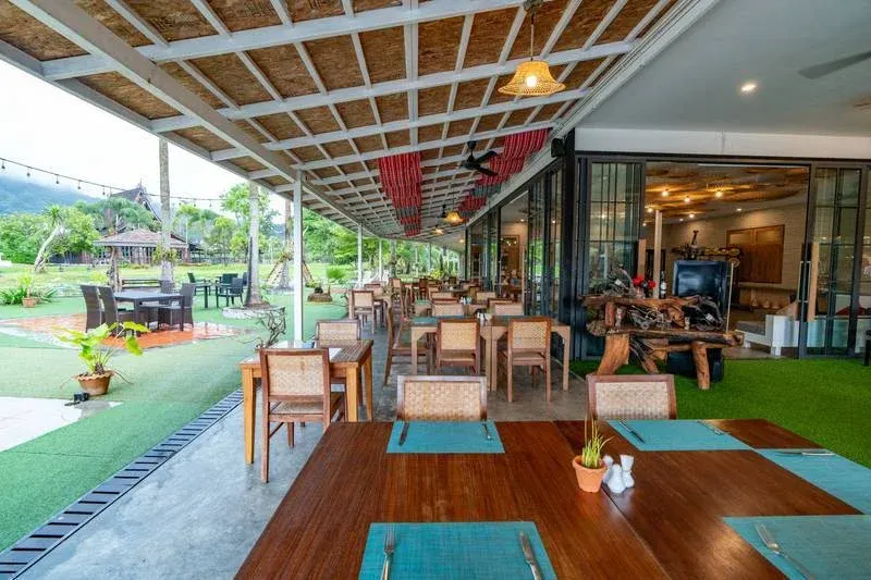 Covered open-air terrace of the restaurant at Naina Resort & Spa, with wooden tables looking onto the garden
