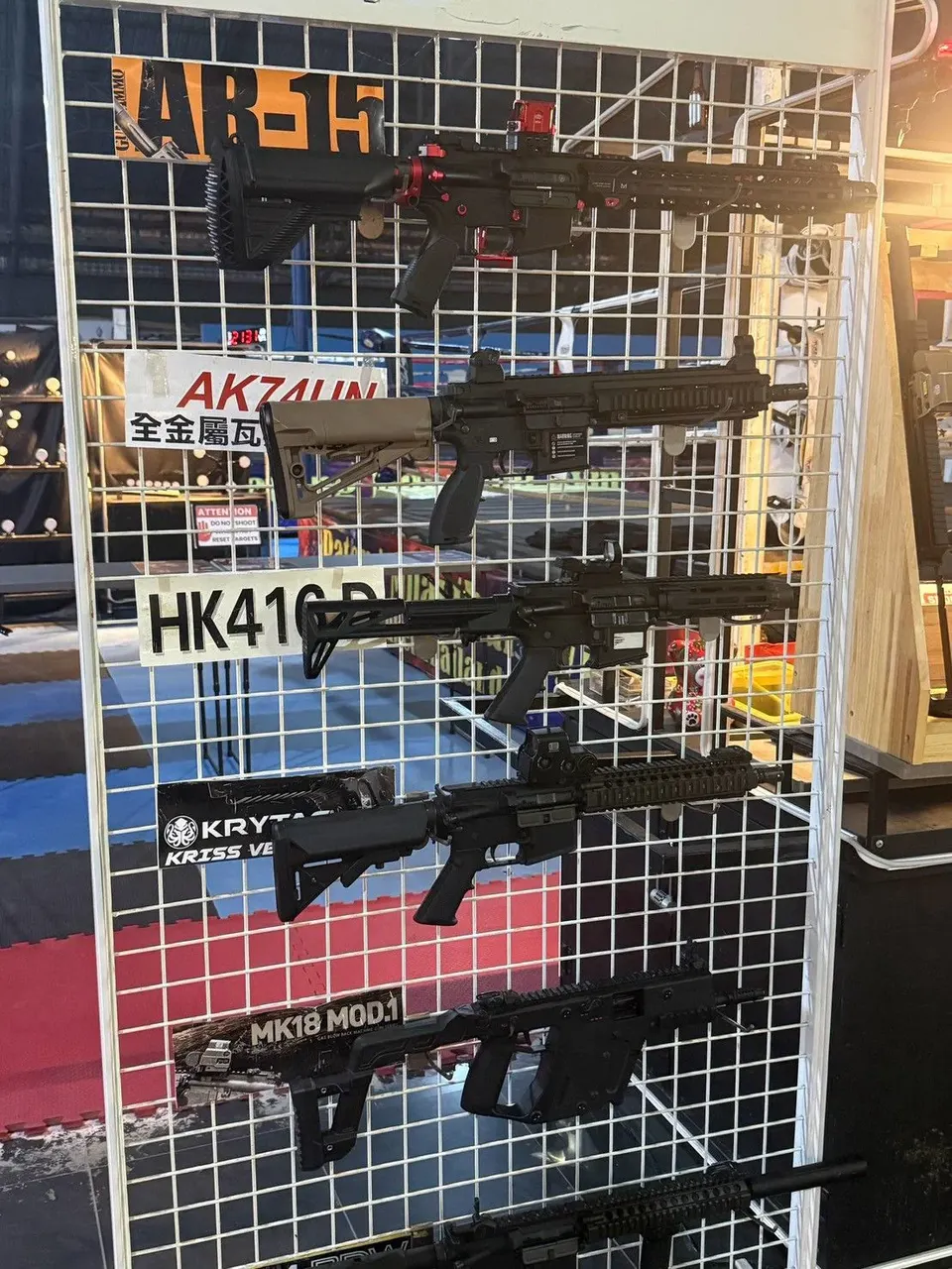 Replica rifles hanging on a wire rack, each with a name card such as AR-15, HK416 D and MK18 MOD.1