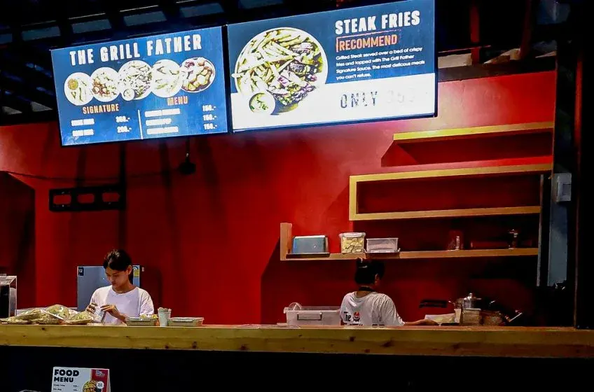 The grill counter inside the stadium, with menu screens showing signature dishes and steak fries above the kitchen staff