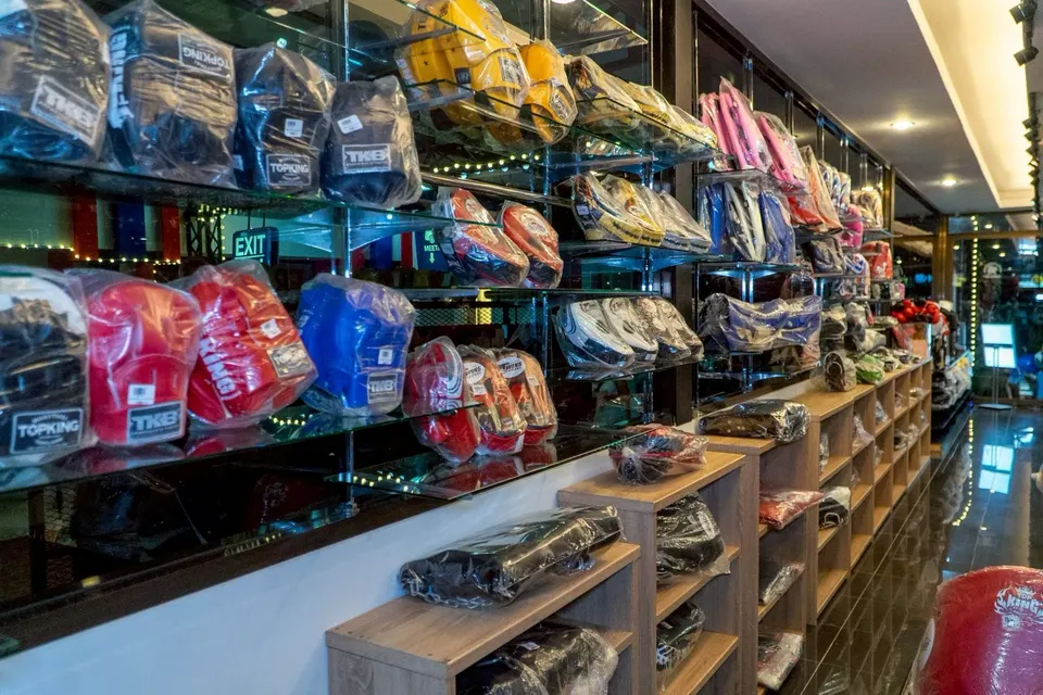 Glass shelves of boxing gloves and pads in plastic wrap, from brands such as Top King and Twins