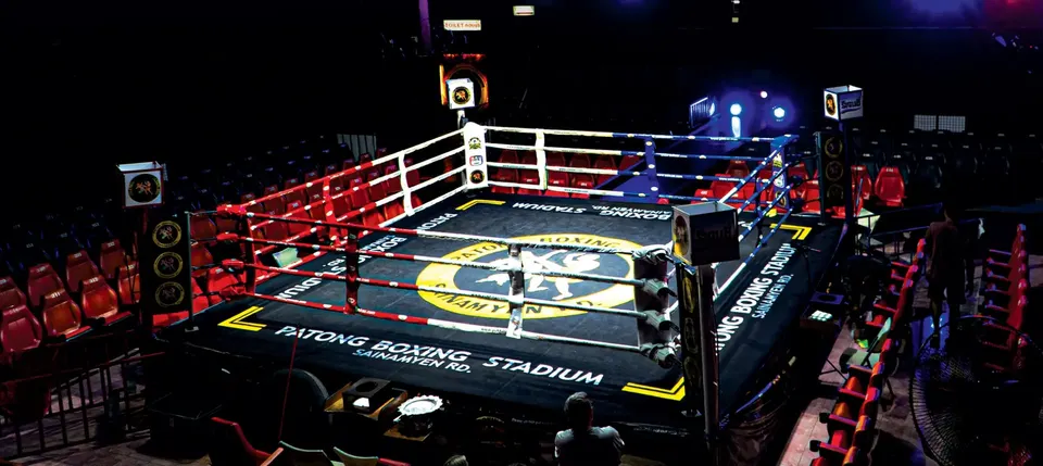 The empty ring with PATONG BOXING STADIUM SAINAMYEN RD. on the apron, surrounded by red seats